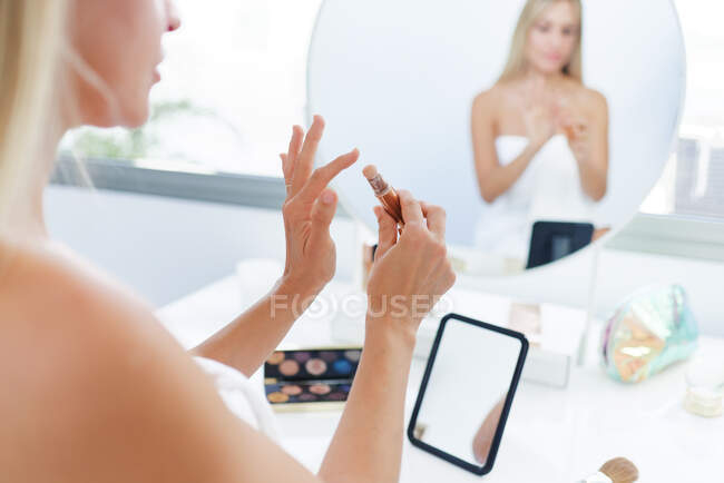 Colheita fêmea sentada à mesa com espelho e aplicando corretor pau enquanto faz maquiagem em casa — Fotografia de Stock