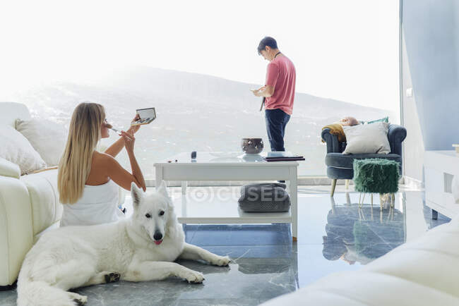 Peaceful female applying eyebrow pencil while doing makeup in room with fluffy dog and boyfriend — Stock Photo