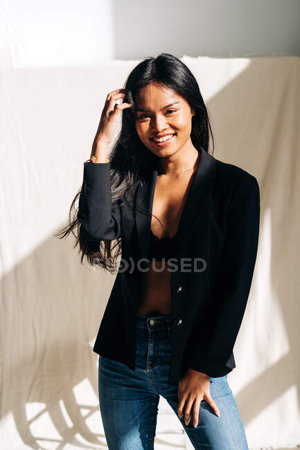 Молода жінка, яка посміхається привабливій латиноамериканській, одягнена в чорну куртку в сучасній світлій кімнаті і озирається. — стокове фото