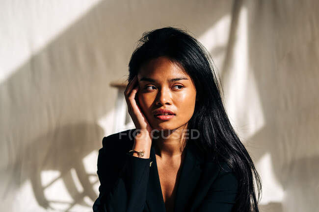 Молодая привлекательная латиноамериканка в черной куртке в современной светлой комнате и смотрит в сторону — стоковое фото