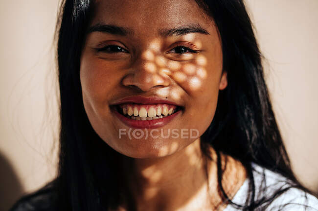 Attractive cheerful young Hispanic woman wearing white cloth looking at camera in sun shadow — Stock Photo