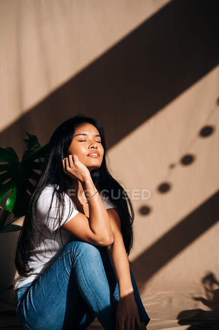 Attractive young Hispanic woman wearing white cloth touching face with eyes closed in sun shadow — Stock Photo