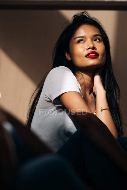 Attractive young Hispanic woman wearing white cloth touching face while looking away in sun shadow — Stock Photo