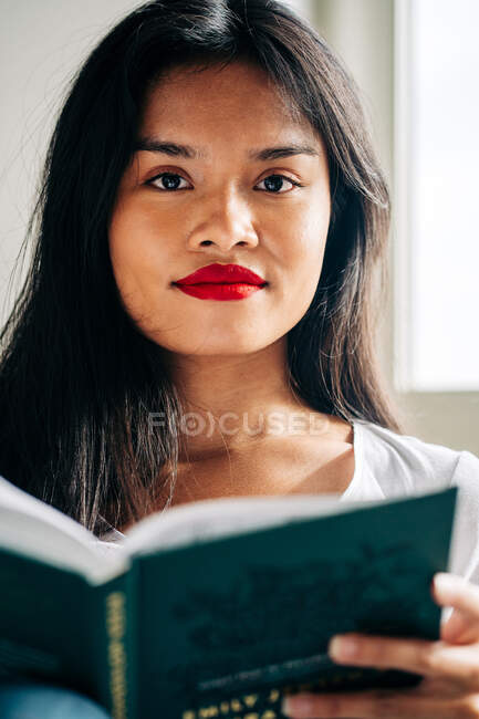 Сконцентрована етнічна студентка в повсякденному одязі сидить на дивані і читає нотатки в блокноті під час навчання — стокове фото