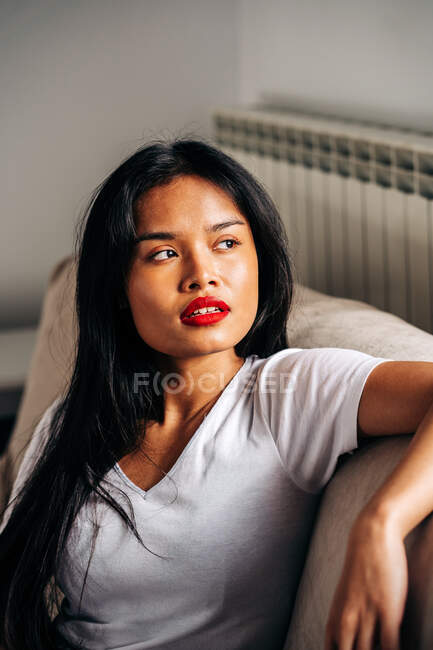 Ritratto su seria femmina etnica seduta su morbido divano distogliendo lo sguardo pur avendo tempo libero — Foto stock