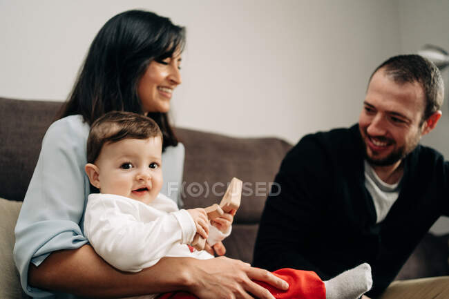 Young father playing with adorable little son sitting on knees of ethnic mother with wooden toy in hands — Fotografia de Stock
