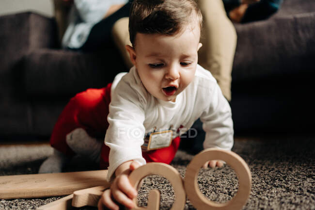 Очаровательный маленький ребенок играет на полу с деревянной игрушкой с буквами имени Тиаго — стоковое фото