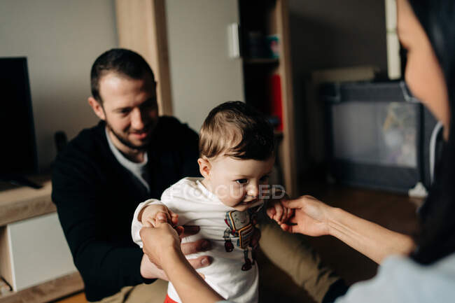Crop unrecognizable happy young parents holding adorable little son doing first steps at home — Photo de stock