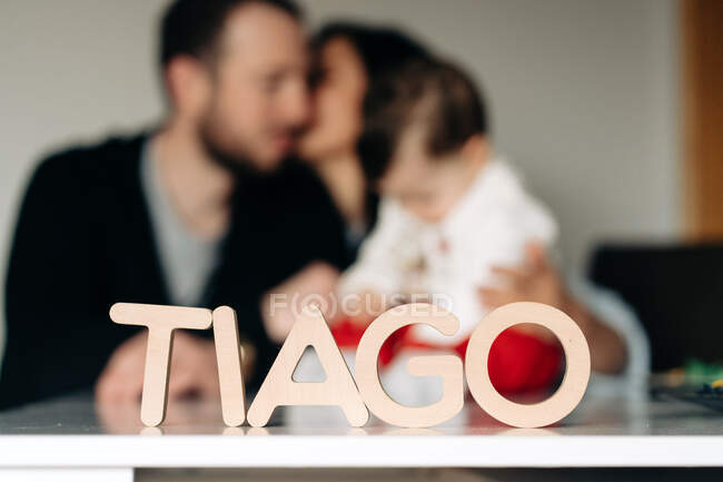 Wooden Tiago letter name placed on table near unrecognizable young parent kissing and embracing little child — Stock Photo