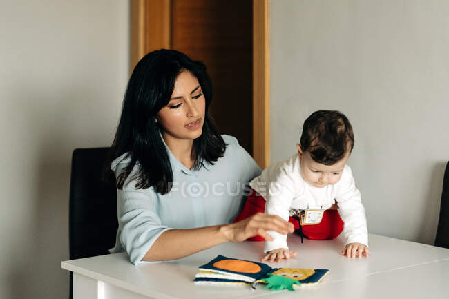Позитивна молода мати і чарівний маленький син, сидячи за столом і читаючи дитячу книгу разом — стокове фото