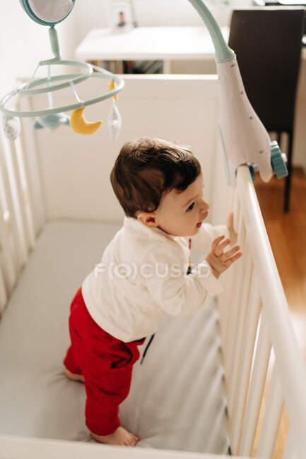 Сверху очаровательный маленький мальчик, стоящий в удобной кроватке — стоковое фото