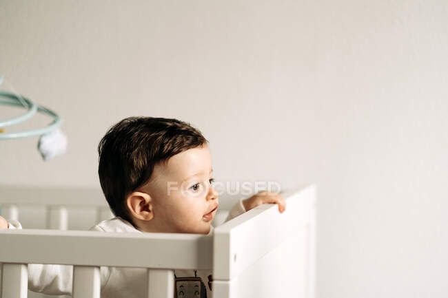 From above adorable little boy standing in comfy crib looking away — Stock Photo