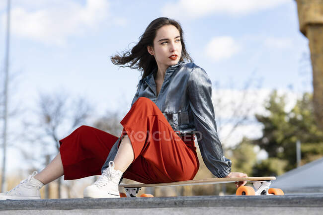 Giovane donna attraente in abiti eleganti seduto sul longboard e guardando altrove — Foto stock