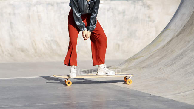 Crop anonymous female in stylish wear riding longboard during training in skate park — Photo de stock