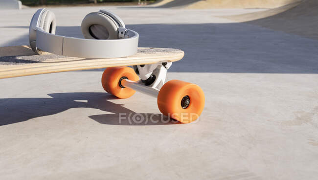 Modernes drahtloses Headset auf Longboard mit hellen Rädern im Skatepark an sonnigen Tagen — Stockfoto