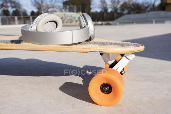 Contemporary wireless headset on longboard with bright wheels in skate park on sunny day — Fotografia de Stock