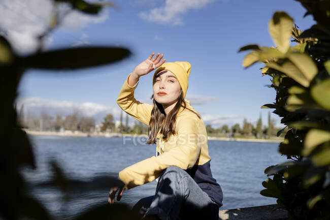 Female adolescent in stylish outfit with makeup looking at camera against lake under blue cloudy sky — Fotografia de Stock