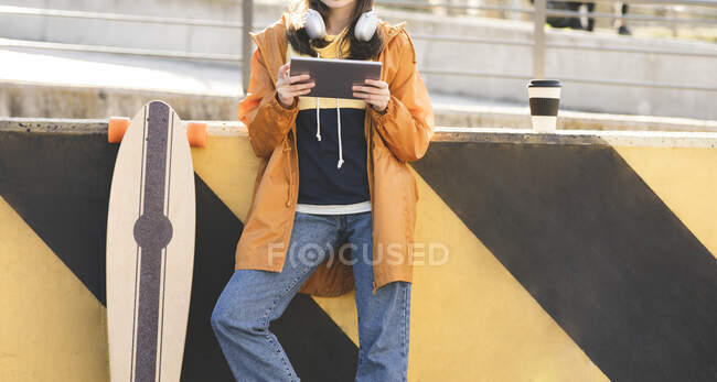 Crop anonymous stylish female browsing internet on tablet near longboard in town on sunny day — Photo de stock