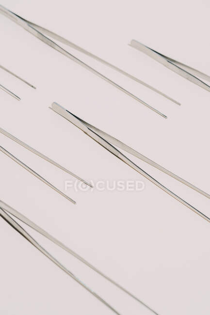 From above of pattern of metal tweezers placed on white background in studio — Photo de stock