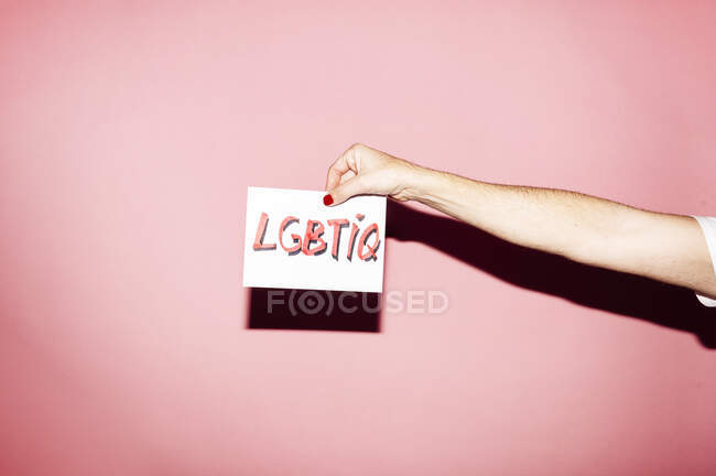 Ernte unkenntlich Homosexuelle Person mit Maniküre demonstriert weißes Papier mit LGBTIQ-Aufschrift vor rosa Hintergrund — Stockfoto