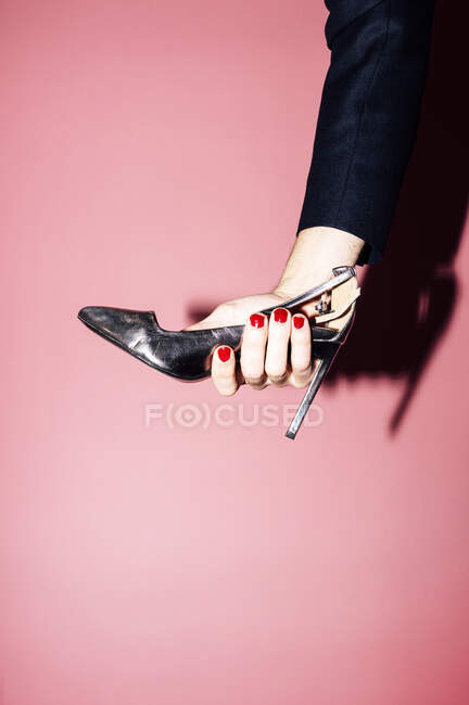 Cropped unrecognizable eccentric homosexual male with red manicure holding high heeled shoe against pink background — Photo de stock