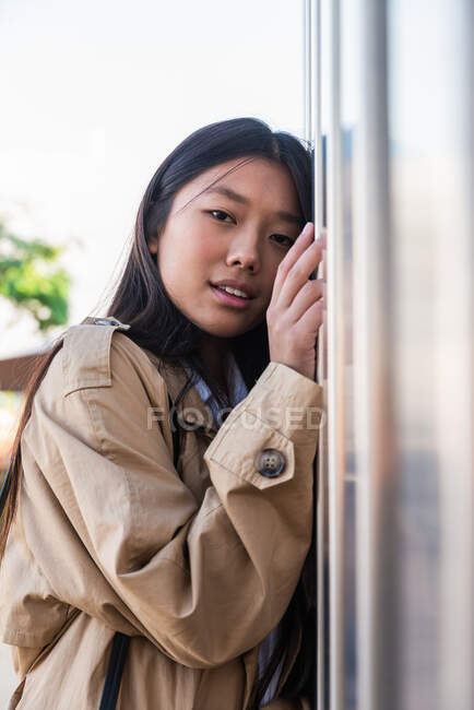 Femmina etnica malinconica in abiti casual con i capelli lunghi guardando la fotocamera mentre si appoggia al muro sulla strada — Foto stock