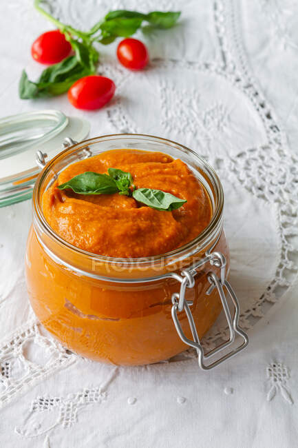 From above full glass jar with homemade natural tomato sauce garnished with fresh green basil leaves placed on table — Photo de stock