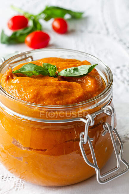 Full glass jar with homemade natural tomato sauce garnished with fresh green basil leaves placed on table — Fotografia de Stock