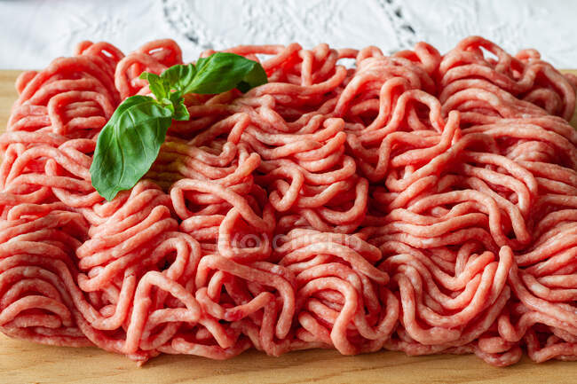 From above of fresh raw mixed pork and beef minced meat on wooden cutting board with green basil leaves placed on table during cooking process — Photo de stock