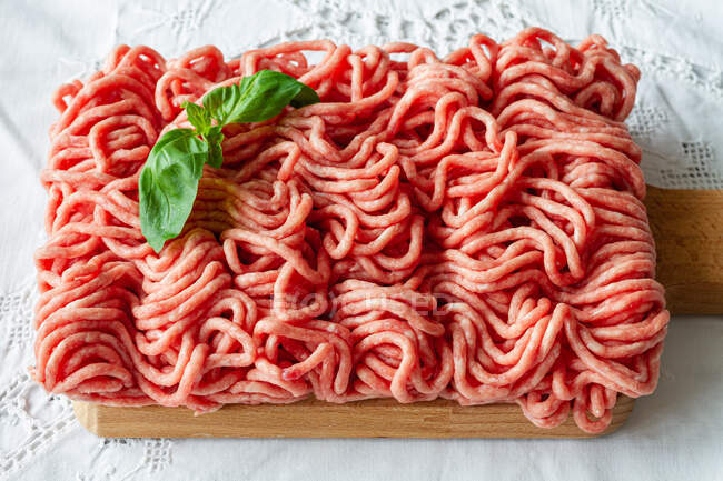 From above of fresh raw mixed pork and beef minced meat on wooden cutting board with green basil leaves placed on table during cooking process — Stock Photo