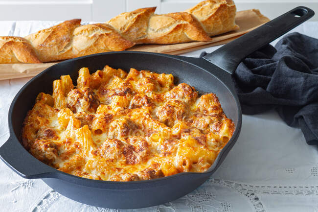 Appetitlich gratinierte Makkaroni mit Frikadellen und Tomatensauce mit Mozzarella, zubereitet und serviert in Pfanne auf dem Tisch mit frischem, knusprigem Brot — Stockfoto