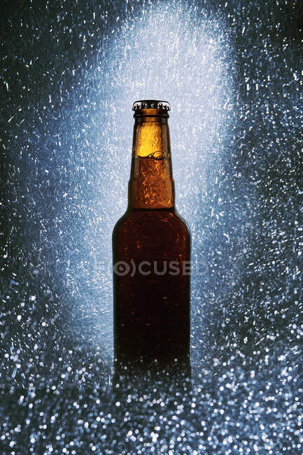 Glass bottle of cold dark beer surrounded by sparkling lights on black background — Stock Photo