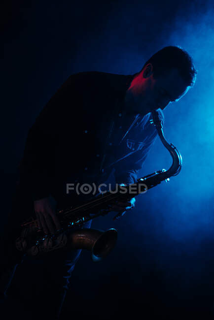 Professional male musician with eyes closed playing saxophone in blue neon lights during live performance — Stock Photo
