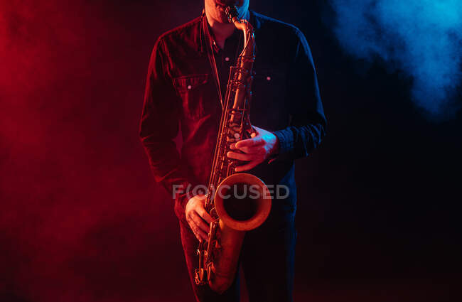 Crop musician playing saxophone in red and blue neon lights during live performance — Photo de stock