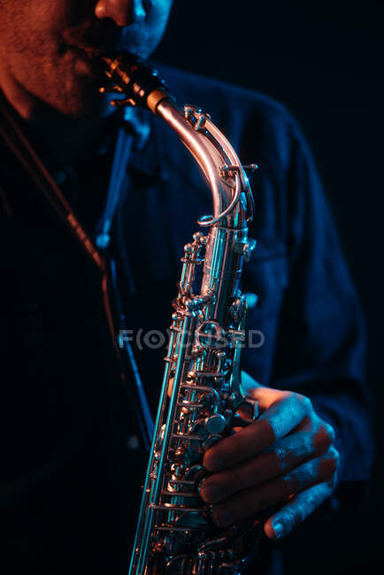 Crop musician with playing saxophone in red and blue neon lights during live performance — Stock Photo
