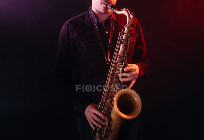 Músico masculino profesional tocando el saxofón en luces de neón rojas durante la actuación en vivo - foto de stock