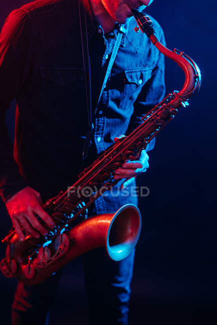 Professional male musician playing saxophone in red and blue neon lights during live performance — Photo de stock