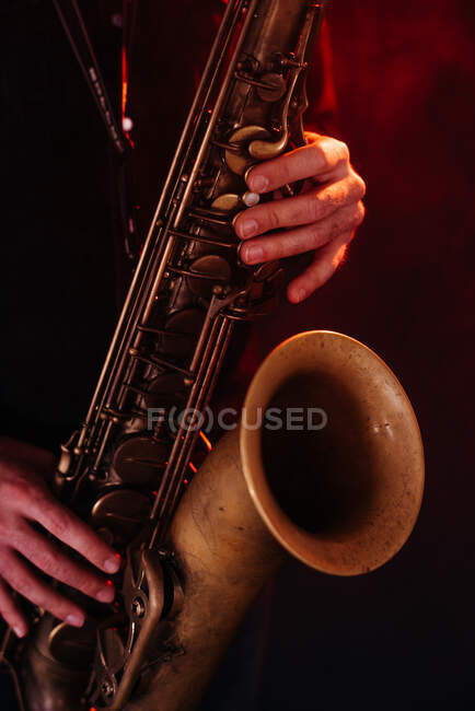 Crop faceless professional musician playing saxophone with fingers on keys during live concert in neon lights — Photo de stock