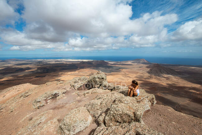 Wanderin in lässigem Outfit sitzt auf felsigem Hügel und genießt weiträumiges Hügelland an klaren Tagen — Stockfoto