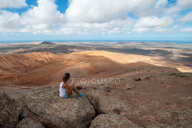 Wanderin in lässigem Outfit sitzt auf einem felsigen Hügel und genießt an klaren Tagen das weite hügelige Tal — Stockfoto