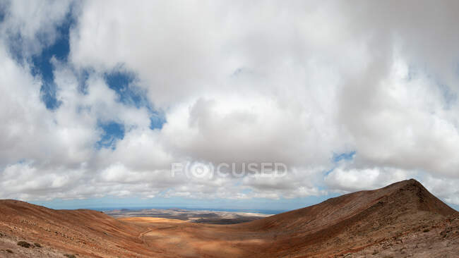 Picturesque scenery of rough hilly seashore near blue sea under blue sky with fluffy clouds — Fotografia de Stock