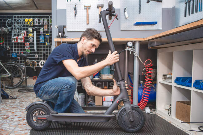 Вид сбоку квалифицированного взрослого мужчины-механика, фиксирующего электрический скутер в современной мастерской — стоковое фото