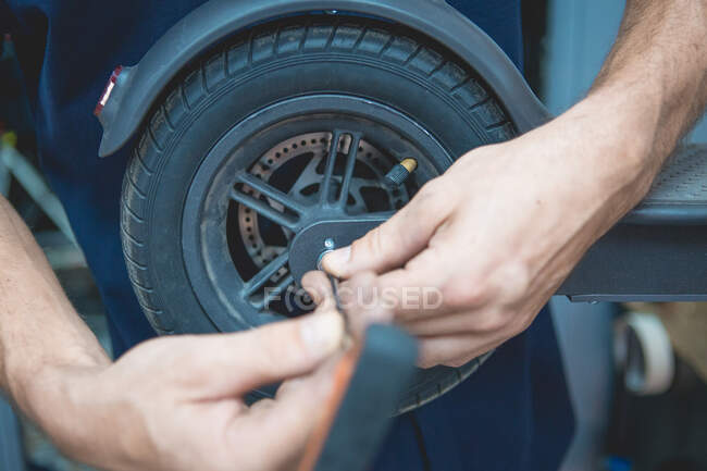 Unbekannter Mechaniker mit Schraubenzieher fixiert Rad von Elektroroller in Werkstatt — Stockfoto