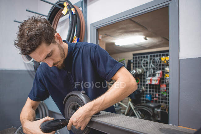 Side view of male mechanic with screwdriver fixing wheel of electric scooter in workshop — Stock Photo