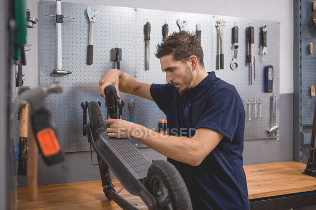 Вид сбоку мужчины с отверткой, закрепляющей колесо электроскутера в мастерской — стоковое фото