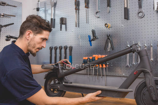 Side view of adult bearded male master attaching details of custom electric scooter while working in professional workshop — Stock Photo