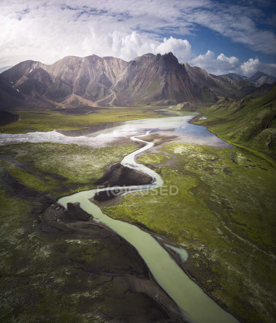 Increíble vista del bucle del río azul curvado que fluye en terreno montañoso áspero cubierto con abundante vegetación exuberante en Islandia - foto de stock