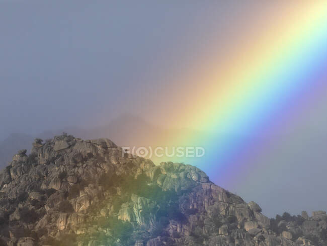 Яркая радуга на облачном небе над горным хребтом — стоковое фото