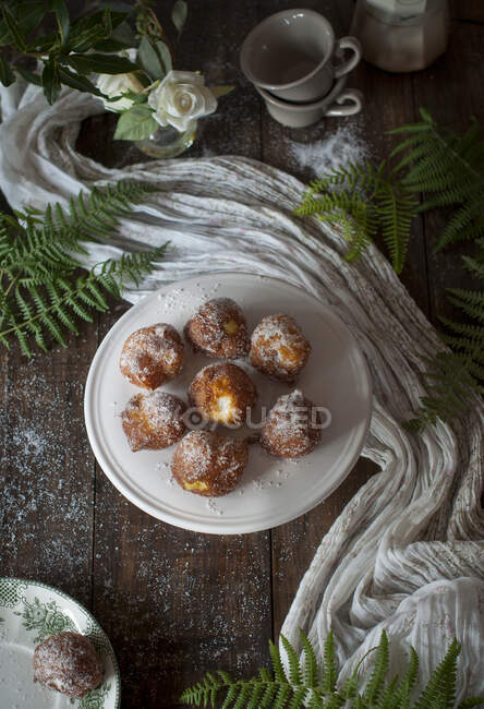 From above homemade custard cream fritters covered with sugar on rustic wooden table with table cloth and leafs decoration — Stock Photo
