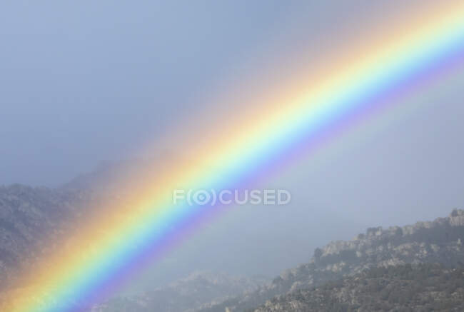 Lebendiger Regenbogen am bewölkten Himmel über dem Bergrücken — Stockfoto